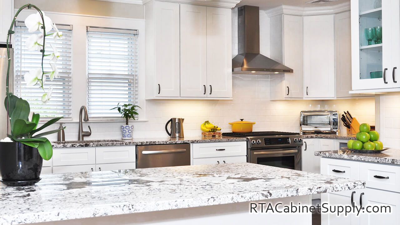 Newport White Shaker kitchen close up view with an island, a countertop, a range hood, a glass door cabinet, wall and base cabinets.