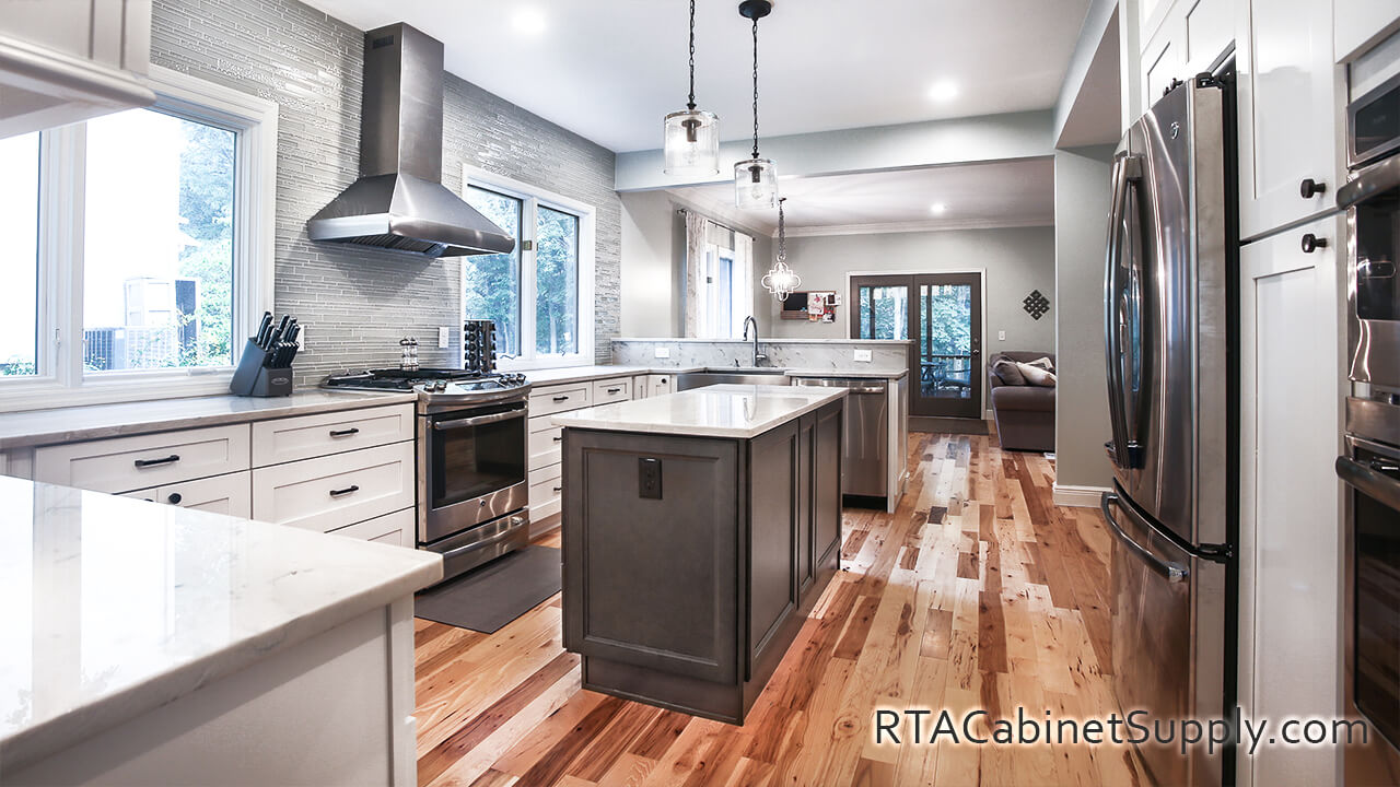 Newport White Shaker kitchen angle view with an island, a fridge, a countertop, a range hood, lighting, wall and base cabinets.