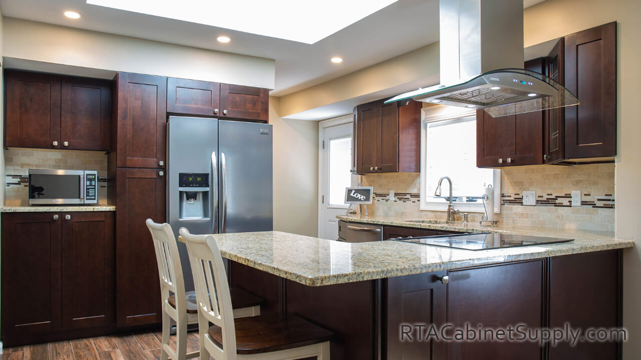 Sienna Shaker kitchen angle view with a fridge, pantry cabinets, a glass door cabinet, a countertop, lighting, wall and base cabinets.