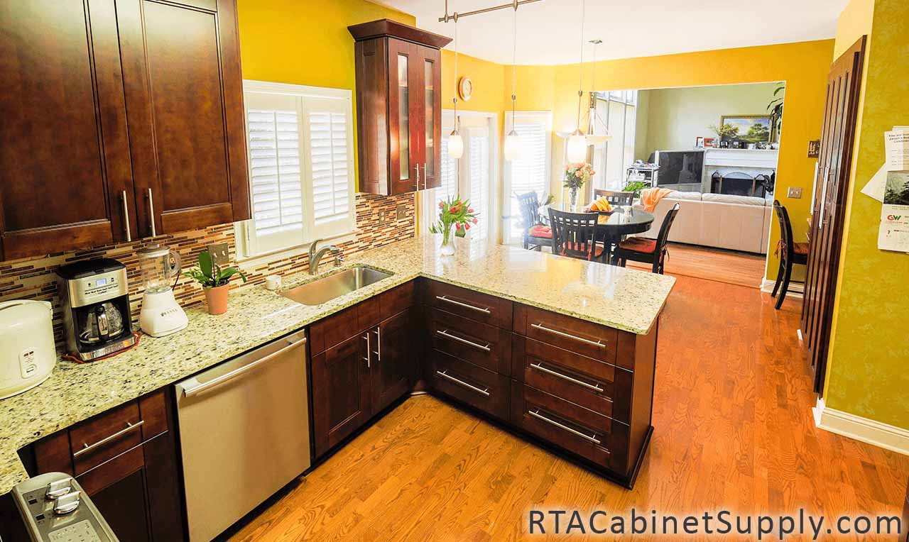 Walnut Shaker kitchen angle view with a glass door cabinet, a countertop, a dining table, lighting, wall and base cabinets.