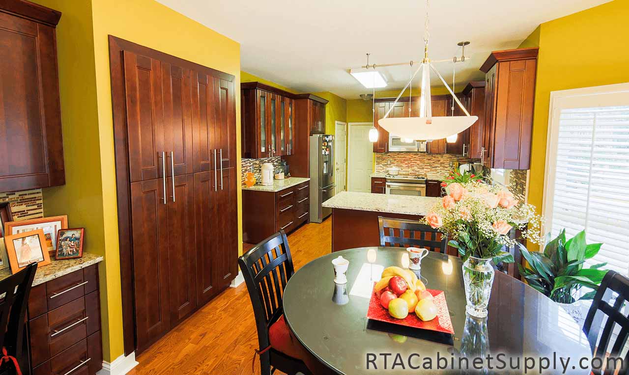 Walnut Shaker kitchen full view with glass door cabinets, a countertop, an oven, a fridge, a dining table, wall and base cabinets.