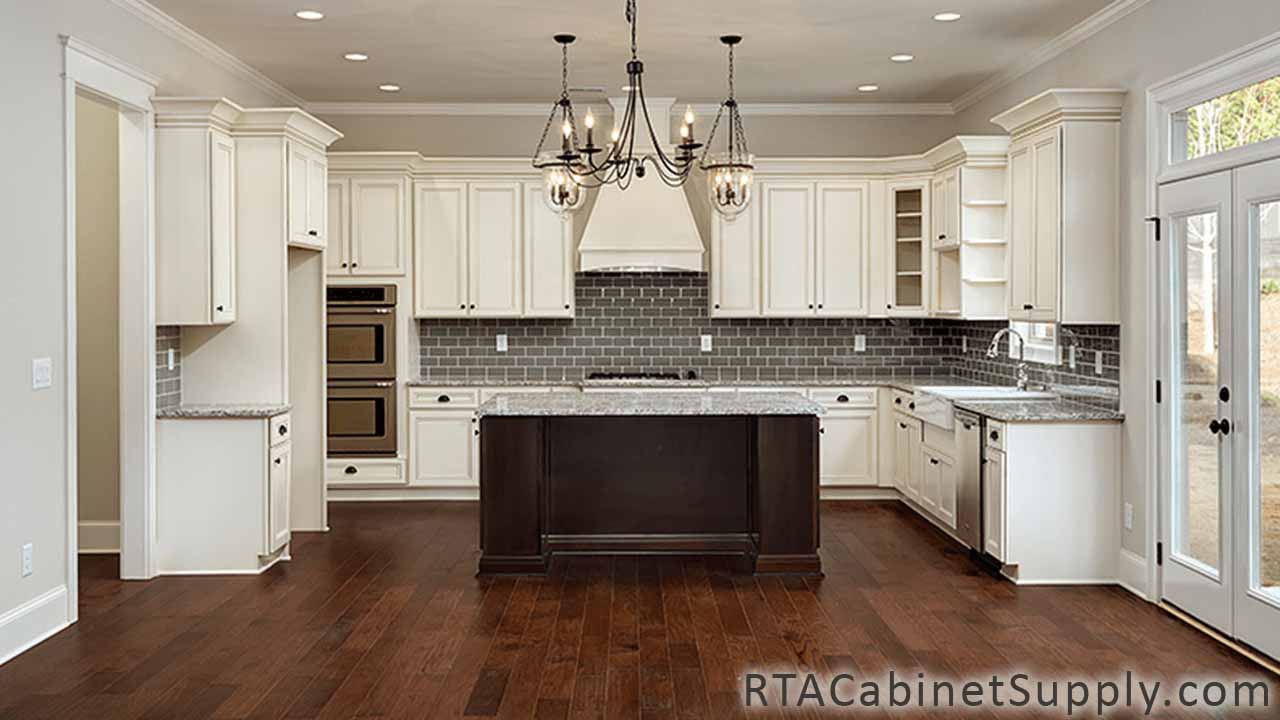 Antique White kitchen full view with an island, lighting, a range hood, a glass door cabinet, wall and base cabinets.