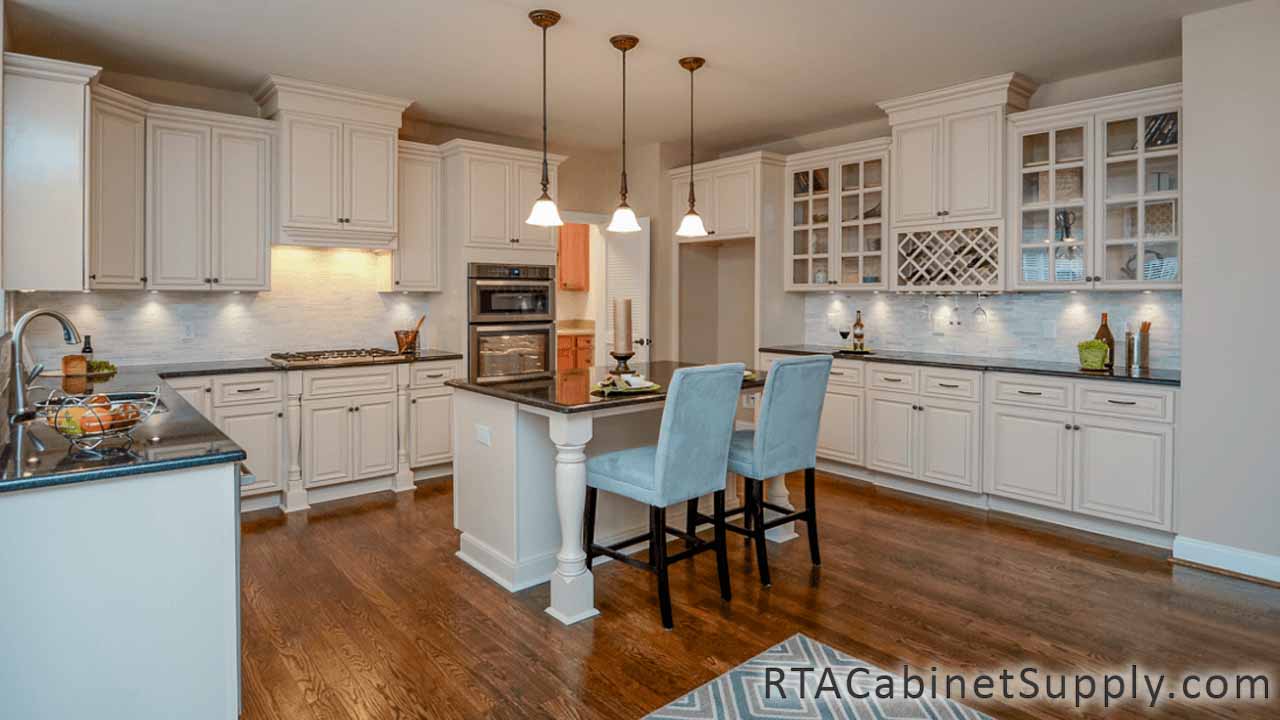 Country Cream kitchen full view with an island, two chairs, a wine rack cabinet, glass door cabinets, wall and base cabinets, lighting.