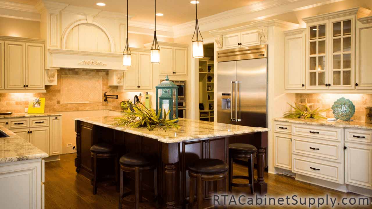 Country Cream kitchen angle view with an island, a range hood cover, a glass door cabinet, wall and base cabinets, and lighting.