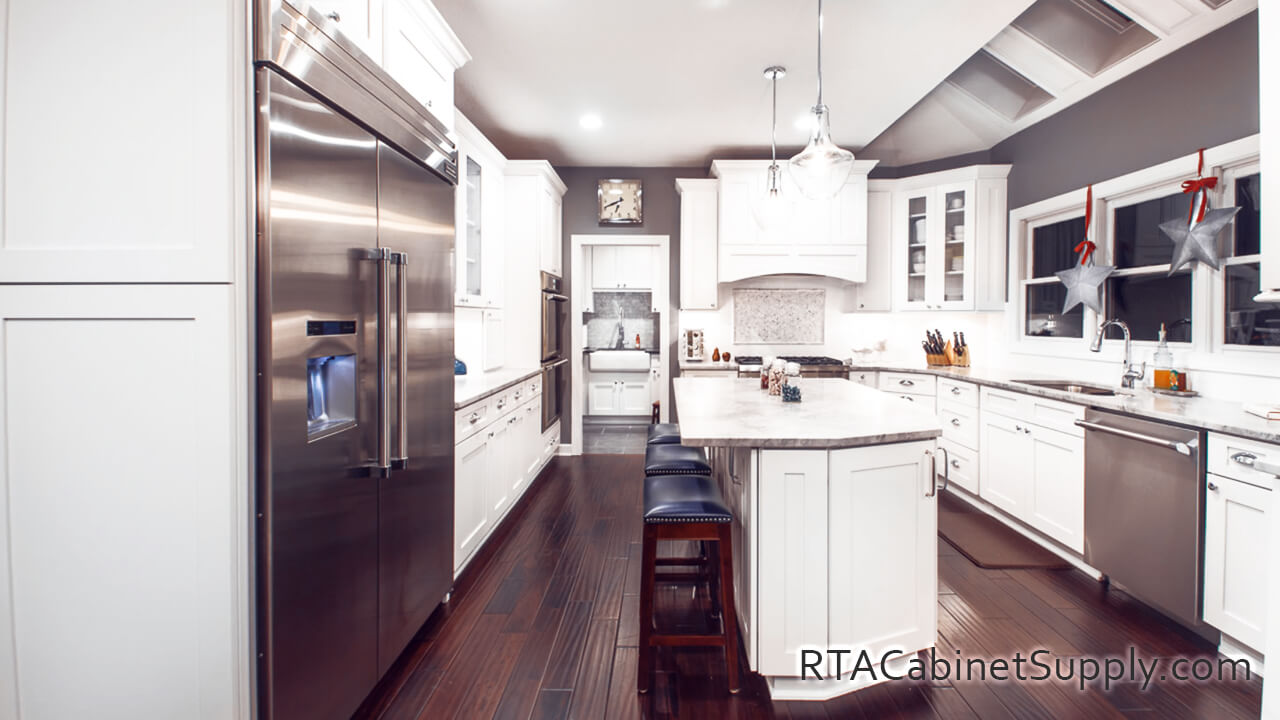 Newport White Shaker kitchen full view with an island, a countertop, a fridge, lighting, glass door cabinets, wall and base cabinets.